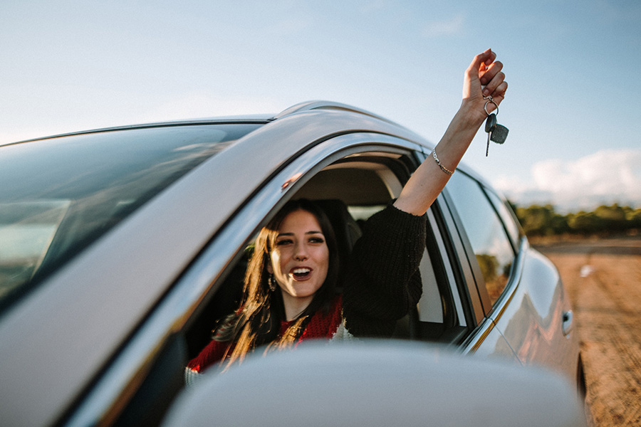 Frau sitzt Glücklich in einem Auto und hält die Schlüssel in die Luft